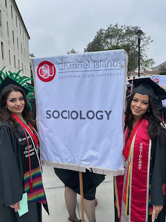 Two students in regalia holding sociology flag